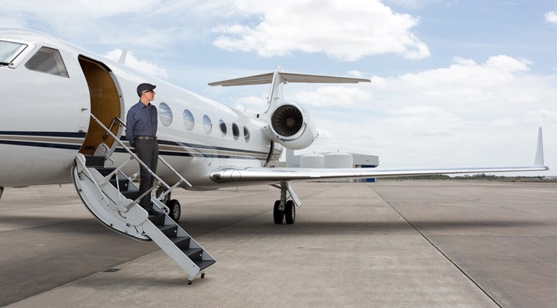 Man standing on the stairs of a private jet wearing a hat